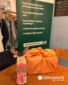 Photo montrant un cadeau emballé dans une étoffe orange et un petit renne de Noël en bois décoratif.